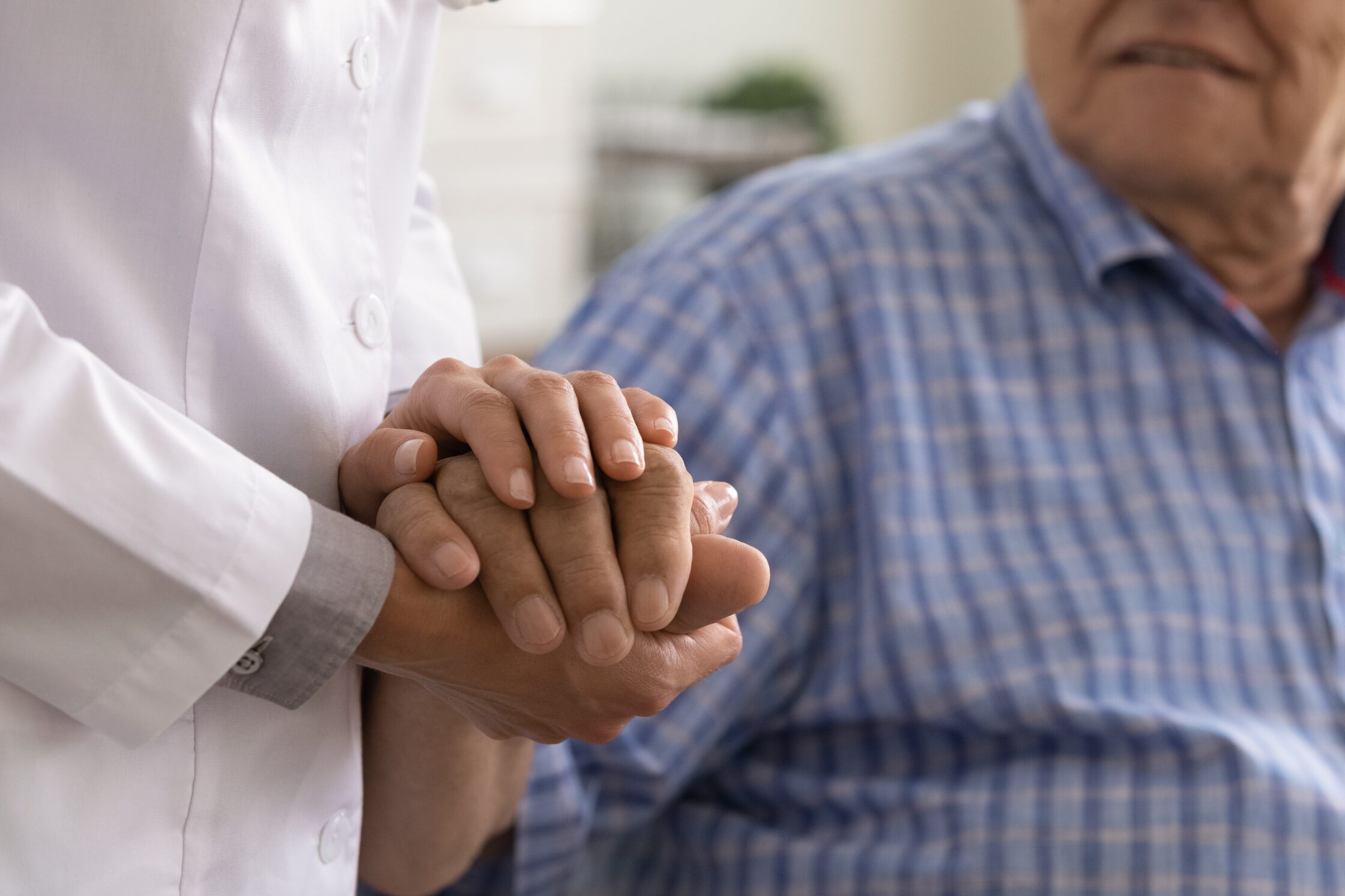 Close up caregiver holding mature man hand, psychological help