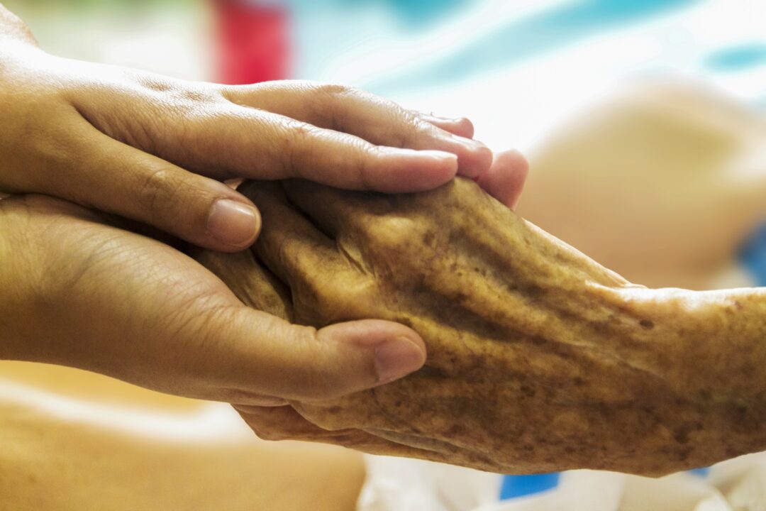 Close up caregiver holding mature man hand, psychological help